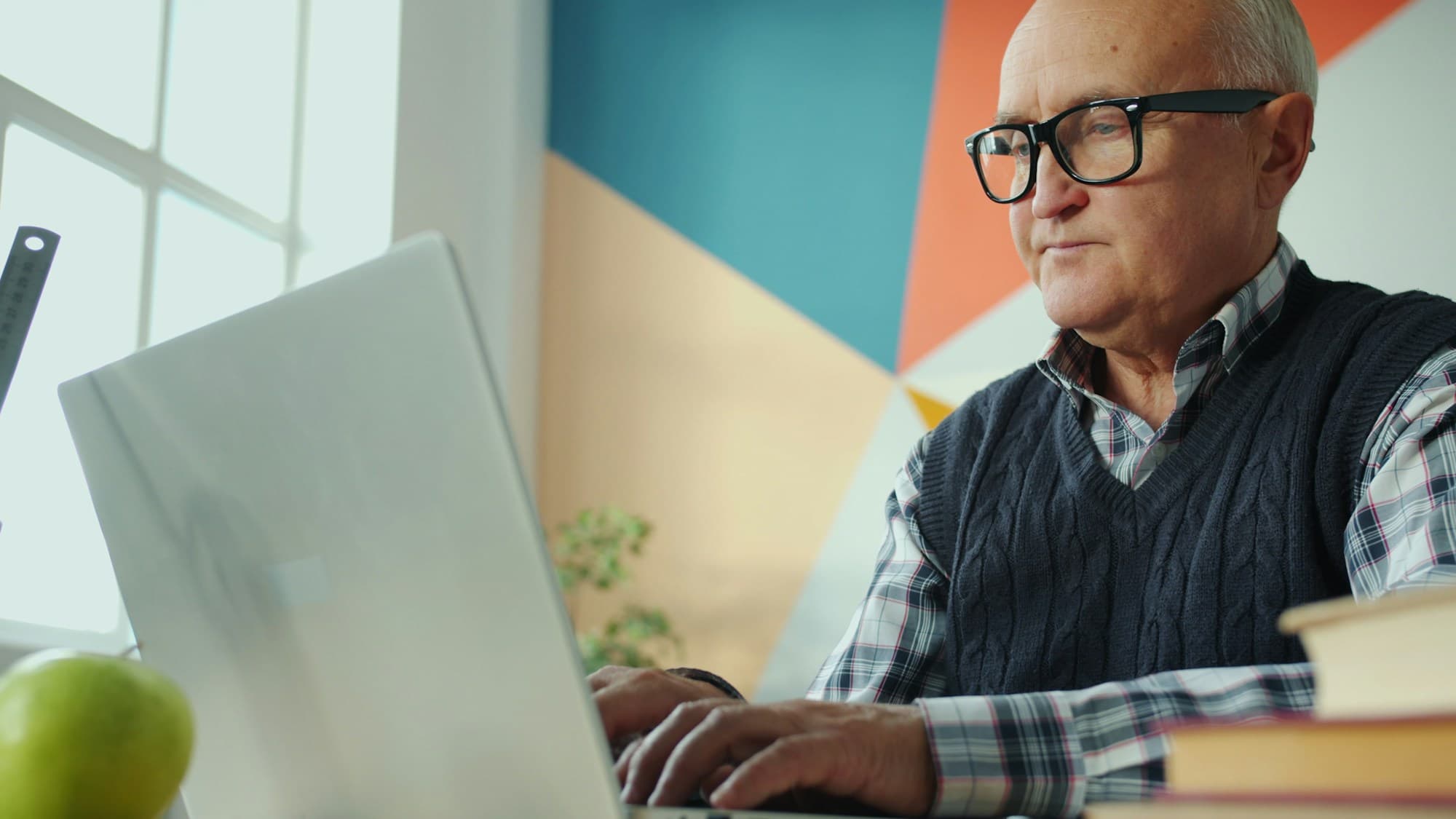 Un homme portant des lunettes travaille à l'ordinateur devant un mur coloré